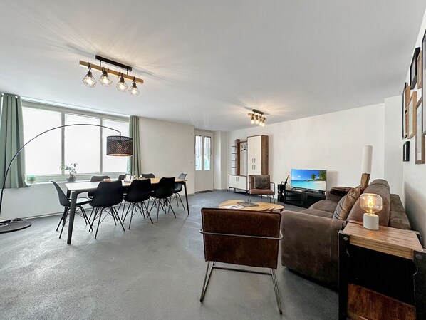 Uma sala de estar moderna com área de jantar, televisão e sofá.