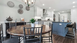 A modern kitchen with a central island, white cabinetry, and a dining area with a round table and chairs. - Niagara Retreat in the Heart of NWA (Springdale)