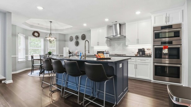 A modern kitchen with a central island, bar stools, stainless steel appliances, and white cabinetry. - Niagara Retreat in the Heart of NWA (Springdale)