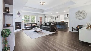 A modern living room with a fireplace, a sofa, a coffee table, and a dining area with bar stools. - Niagara Retreat in the Heart of NWA (Springdale)