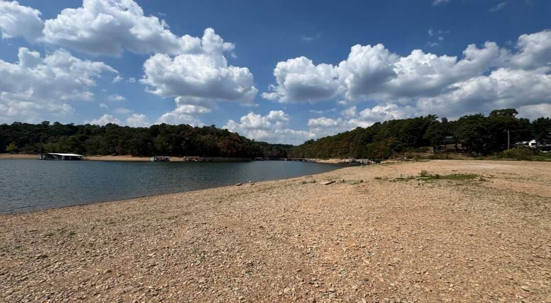 A riverbank with a gravel path, a small boat, and a forested area in the background.