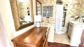 Een badkamer met een houten wastafelmeubel, twee spiegels, een douche met glazen deur en een betegelde spatwand.