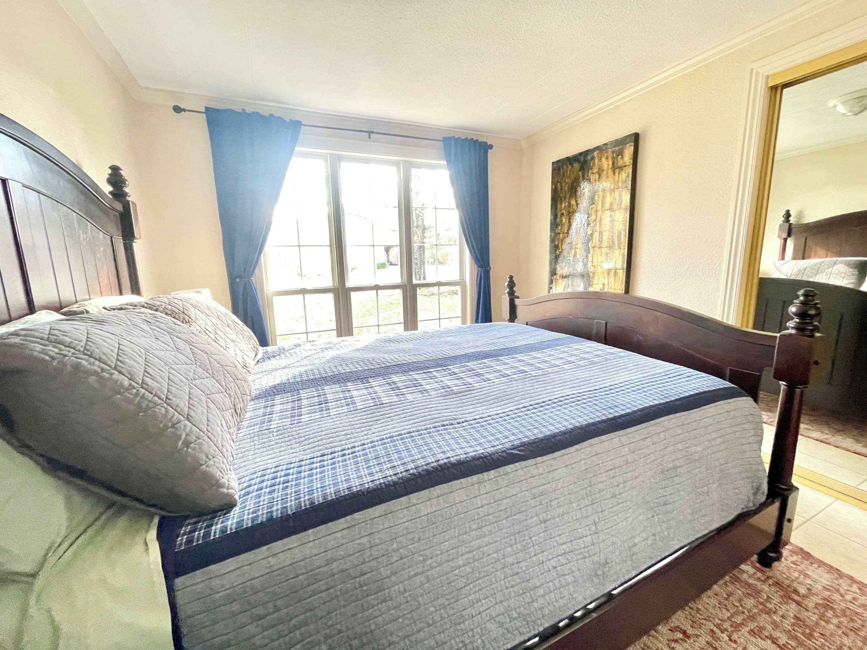 A bedroom with a bed, a window with curtains, a painting on the wall, and a wooden headboard.