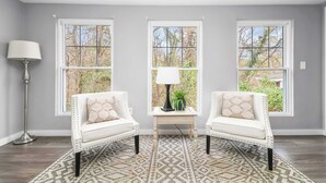 Una habitación con dos sillones blancos, una mesita con lámpara y un tapete estampado.