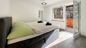 Ein Schlafzimmer mit Bett, Fenster und einer Tür, die zu einem Außenbereich führt.