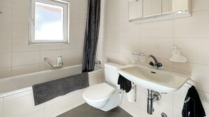 Ein modernes Badezimmer mit Badewanne, Toilette, Waschbecken und einem Fenster.