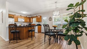 A modern kitchen with wooden cabinets, a central island, bar stools, and a dining table with chairs. - Beaver Lake Getaway - Fenced Yard, Pets OK (Springdale)