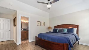 A bedroom with a wooden bed, a ceiling fan, and a bathroom visible through an open door. - Beaver Lake Getaway - Fenced Yard, Pets OK (Springdale)