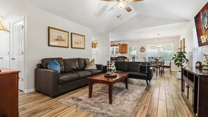 A living room with a brown leather sofa, a wooden coffee table, and a ceiling fan. - Beaver Lake Getaway - Fenced Yard, Pets OK (Springdale)