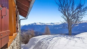 A wooden cabin with a stone exterior, a wooden door, and a view of snow-covered mountains.