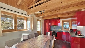 A modern kitchen with red cabinets, a dining area with a table and chairs, and a view of the outdoors through large windows.