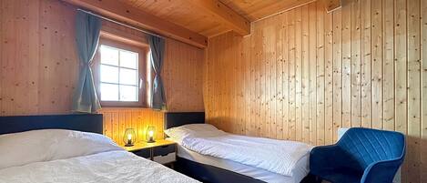 Ett rum med två sängar, en blå stol och ett fönster med gardiner.