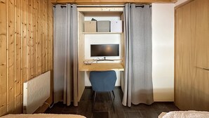 A compact room with a wooden ceiling, a desk with a computer, a chair, and storage shelves.