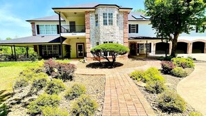 A two-story house with a stone facade, a covered porch, and a well-maintained garden with a central tree. - Enjoy 3 King beds with ensuite baths, 8 total beds (Fayetteville)