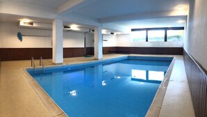 Una amplia piscina interior con agua cristalina azul, rodeada de suelo con baldosas beige y marrones.