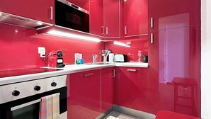 Cocina compacta con armarios rojos, encimera blanca y un pequeño comedor.