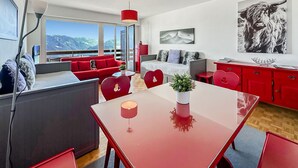 Una sala de estar moderna con un sofá rojo, una mesa de comedor y vistas a montañas a través de amplios ventanales.