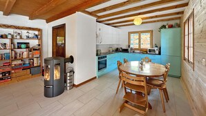 A cozy kitchen with a wood stove, a dining table with chairs, and a bookshelf filled with books and decorative items. - Chalet Albarose - Vercorin (Chalais)