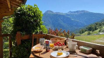 Une table en bois, dressée pour le petit-déjeuner, avec une vue imprenable sur les montagnes.