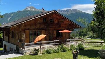 Un chalet rustique en bois, avec des fondations en pierre, une véranda en bois et un parasol rouge.