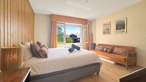 Ein Schlafzimmer mit einem großen Bett, einer Couch, einem Holzboden und einem Fenster mit Vorhängen.