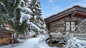 A rustic cabin with a snow-covered roof, a wooden exterior, and a window.