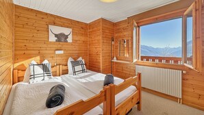 Ein Schlafzimmer einer Holzhütte mit Bett, Fenster mit Bergblick, Holz-Kopfteil und Deckenleuchte.