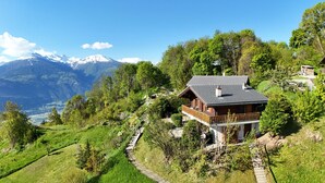 Eine Chalet mit Balkon, umgeben von üppiger Vegetation und einer Bergkulisse.