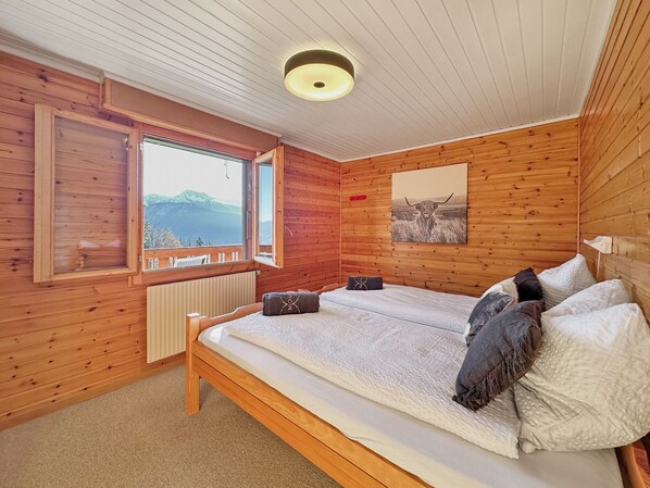 A wooden cabin room with a bed, a window with a view of mountains, and a ceiling light. - The Mirador Lodge - Crans Montana - Swiss Alps (Crans-Montana)