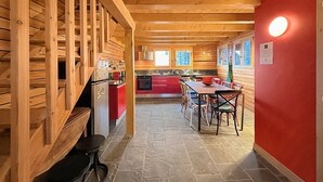 Un intérieur en bois comprenant une cuisine et un coin repas, avec un mur rouge et un sol en pierre.