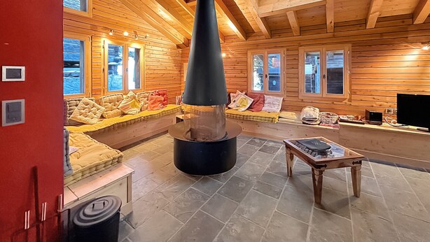 L’intérieur chaleureux d’un chalet avec une cheminée en pierre, des murs en bois et un coin salon confortable.