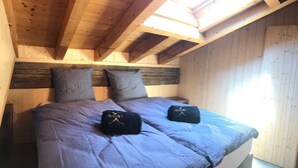 Une chambre de style « loft » avec un plafond en pente, des poutres en bois et une lucarne.