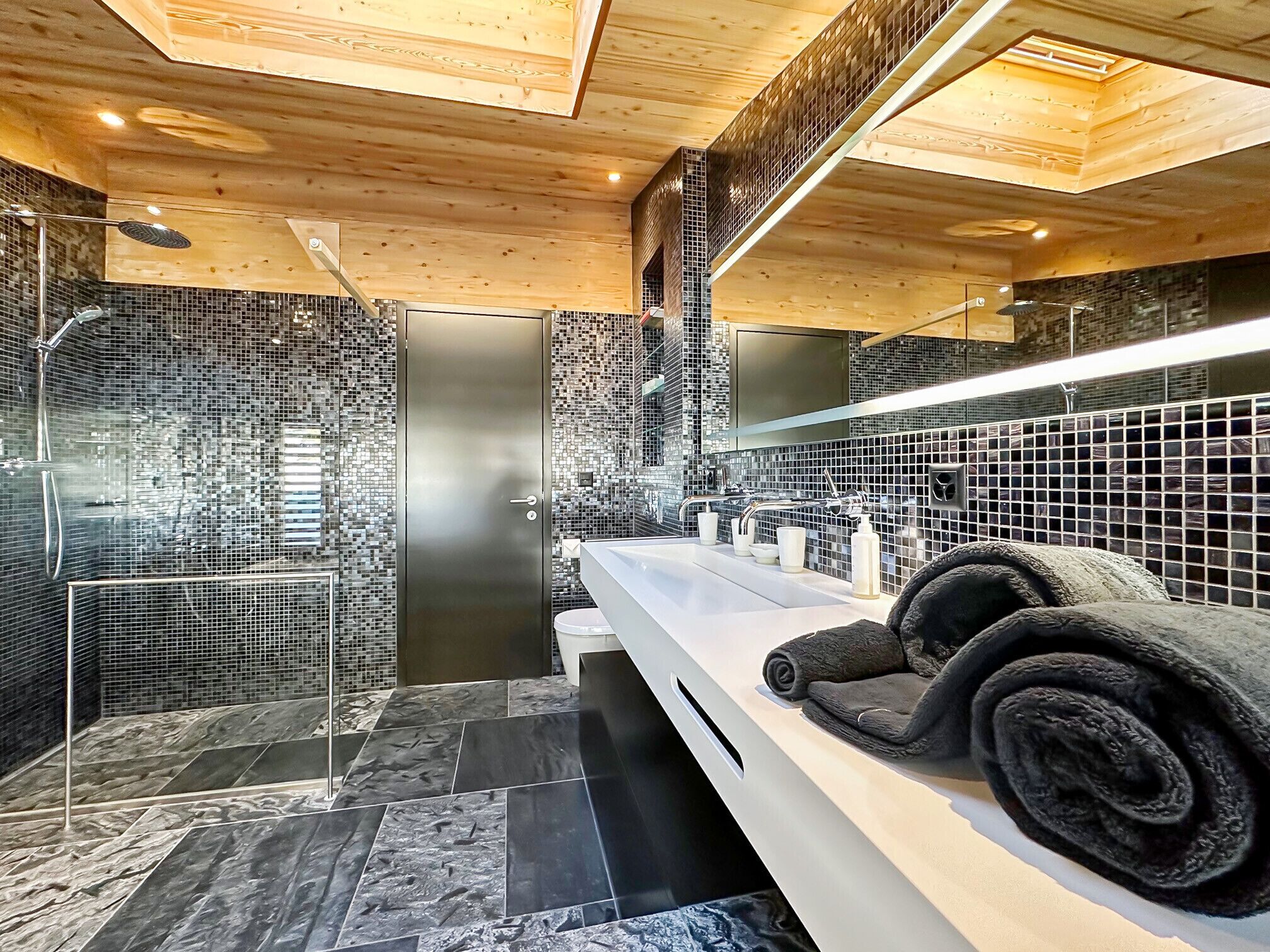 A modern bathroom with a large mirror, a white countertop, and a shower area.