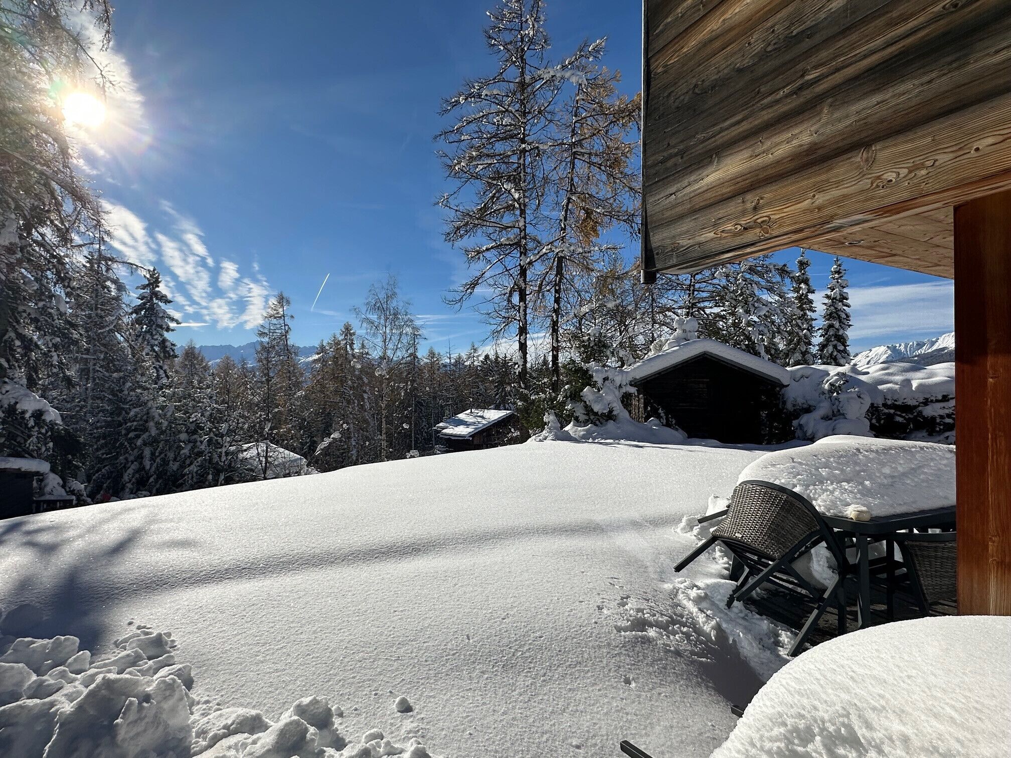 Schneebedecktes Freigelände mit einer Holzhütte, einem Stuhl und einem Tisch.
