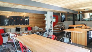 Un interior moderno con techo de madera, un sofá con cojines rojos, una zona de comedor con mesa de madera y una cocina con encimera de madera.
