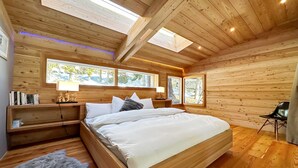 Un dormitorio de cabaña de madera con una cama, mesitas de noche y una ventana con vistas a un bosque.