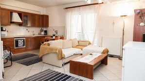 A modern kitchen with wooden cabinets, a built-in oven, and a dining area with a sofa and coffee table. - Cozy apt in Peristeri near Metro station (Peristeri)