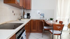 A modern kitchen with wooden cabinets, a built-in oven, a dining table with chairs, and a small potted plant. - Cozy apt in Peristeri near Metro station (Peristeri)
