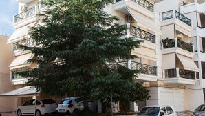 A multi-story building with balconies, parked cars, and a tree in front. - Cozy apt in Peristeri near Metro station (Peristeri)