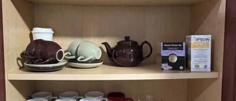 Une étagère de cuisine contenant divers objets, notamment une théière, des tasses et des boîtes.