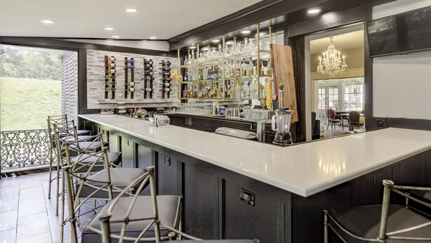 A modern bar area with a long counter, multiple stools, and a variety of glassware and bottles on shelves. - The Inn at Cedar Grove (Vicksburg)