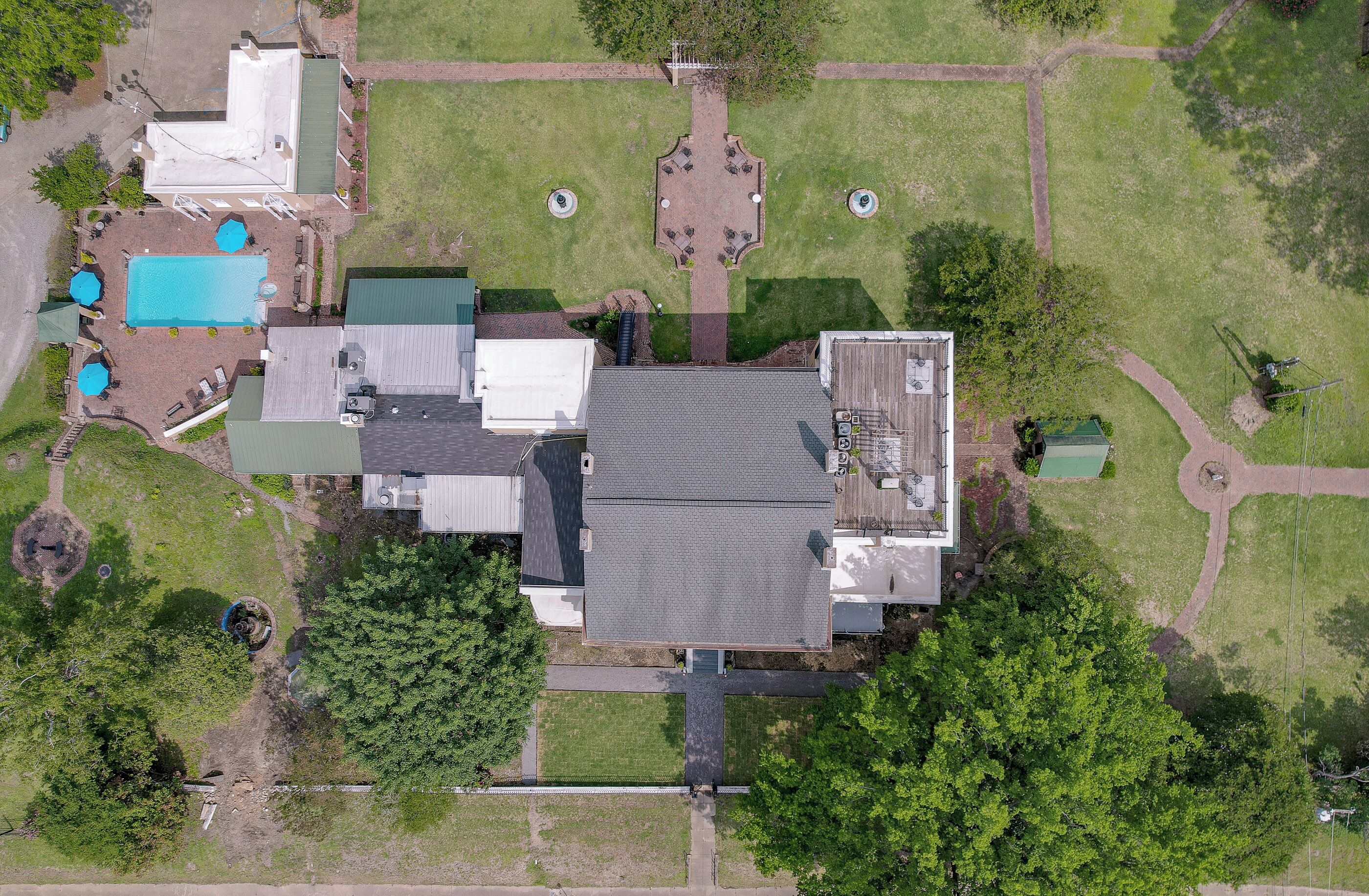 An aerial view of a residential property with a large house, a swimming pool, and a well-maintained lawn.