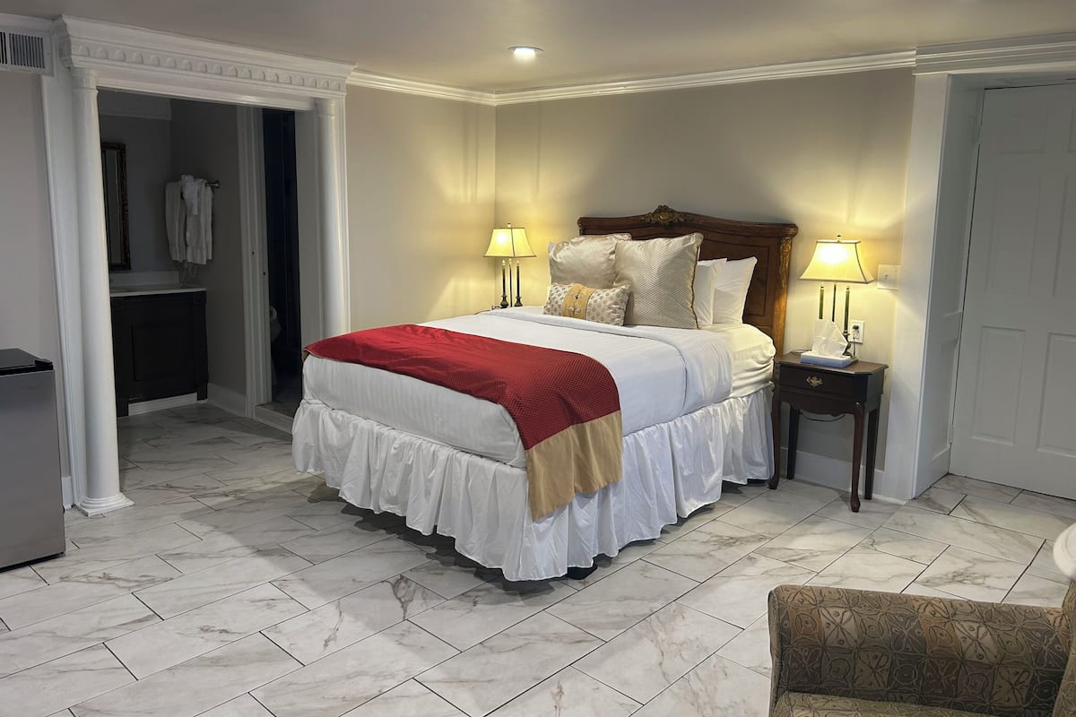A neatly arranged bedroom with a large bed, two bedside lamps, a nightstand, and a chair.