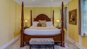 A four-poster bed with a tufted bench in front, a nightstand with a lamp, and a framed painting on the wall.