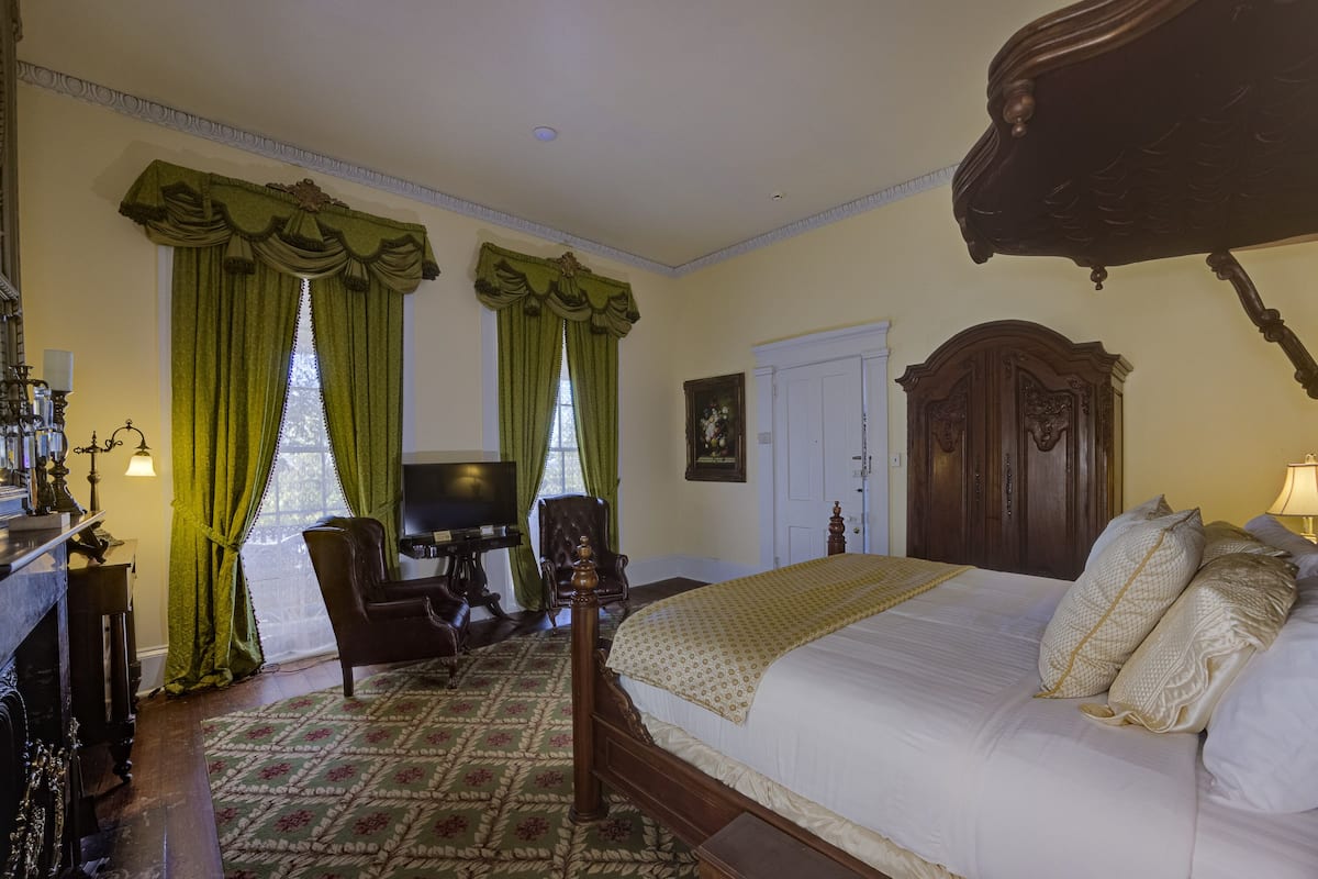 A bedroom with a large bed, green curtains, a wooden wardrobe, and a desk with a chair.