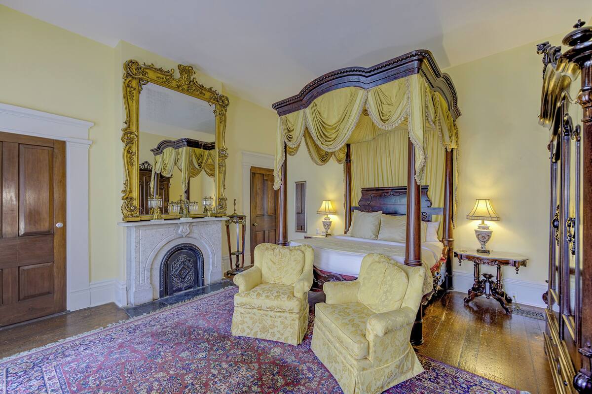 A luxurious bedroom with a four-poster bed, ornate furniture, and a large mirror.