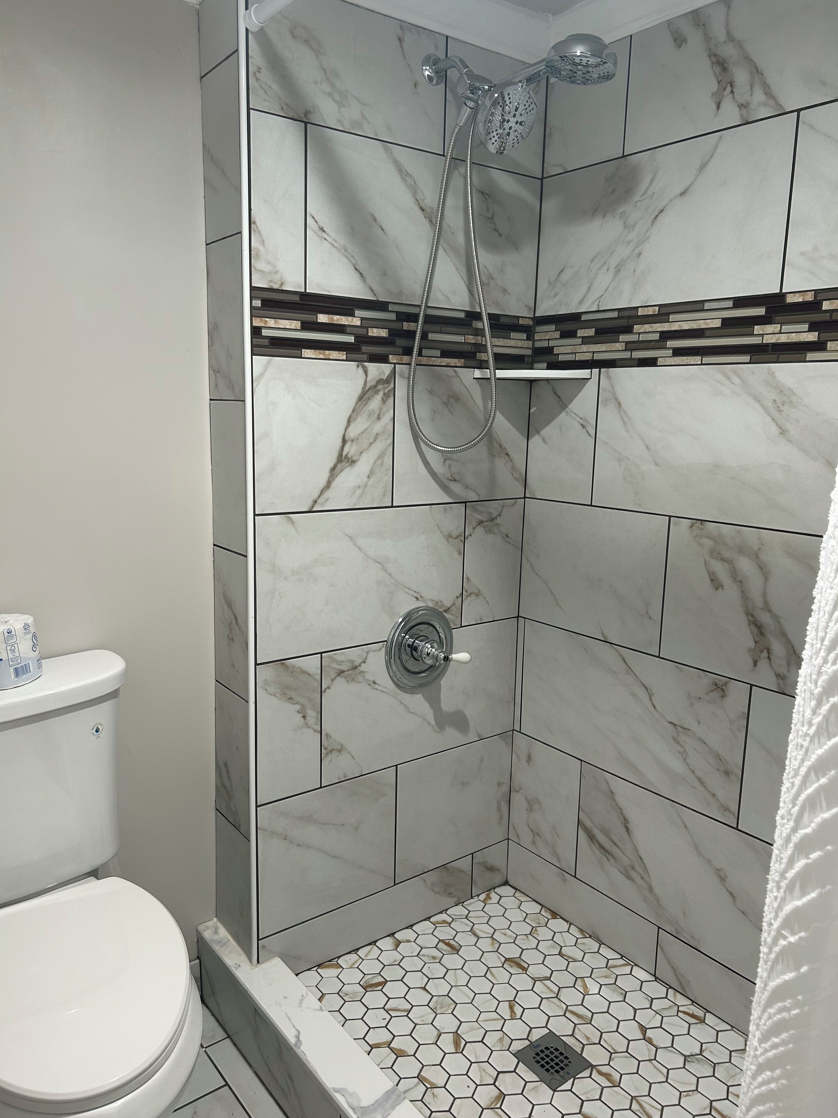 A shower with a handheld showerhead and a wall-mounted faucet.