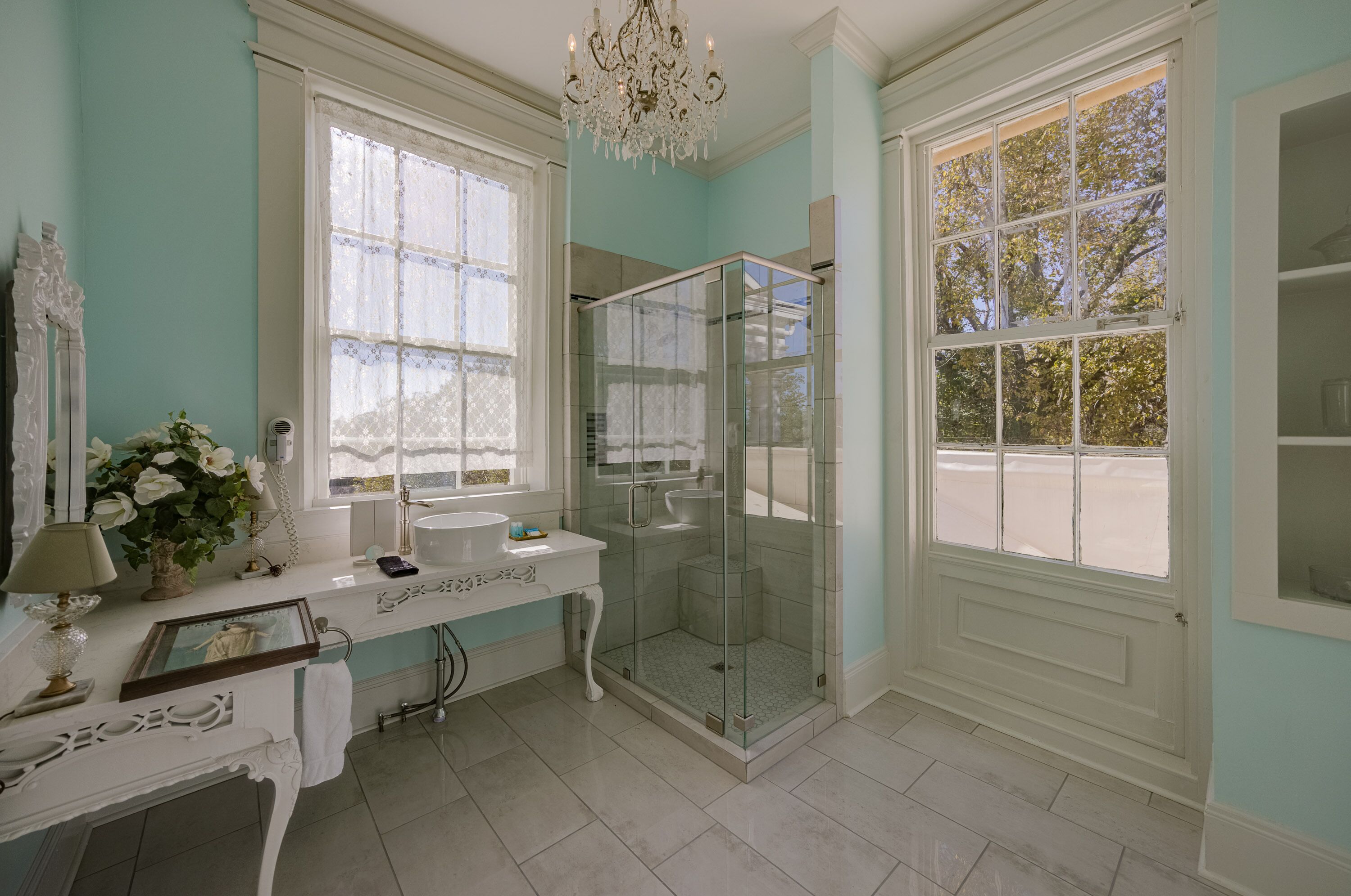 A bathroom with a vanity, a glass-enclosed shower, and large windows.