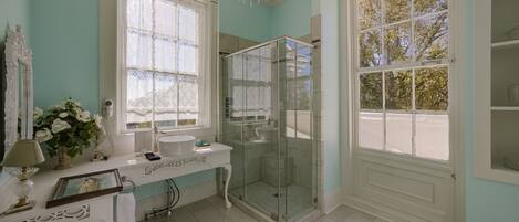 A bathroom with a vanity, a glass-enclosed shower, and large windows.