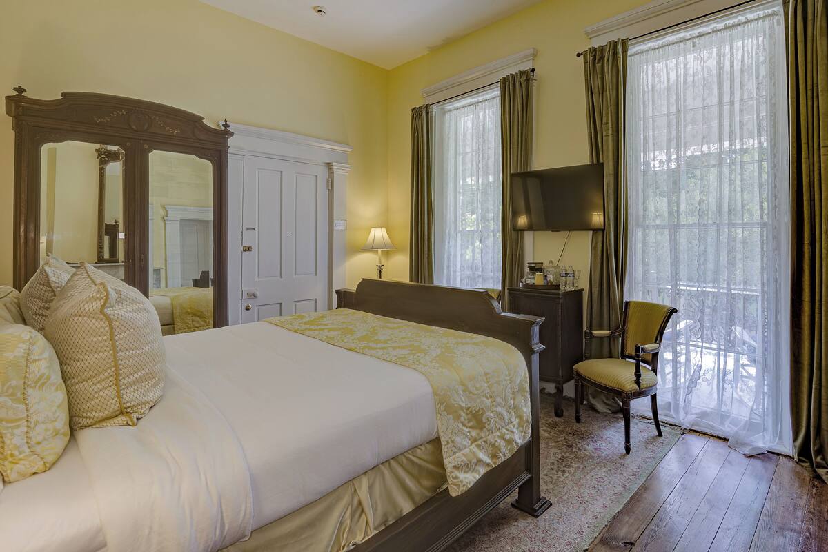 A hotel room with a large bed, a desk with a lamp, a chair, and a large window with curtains.
